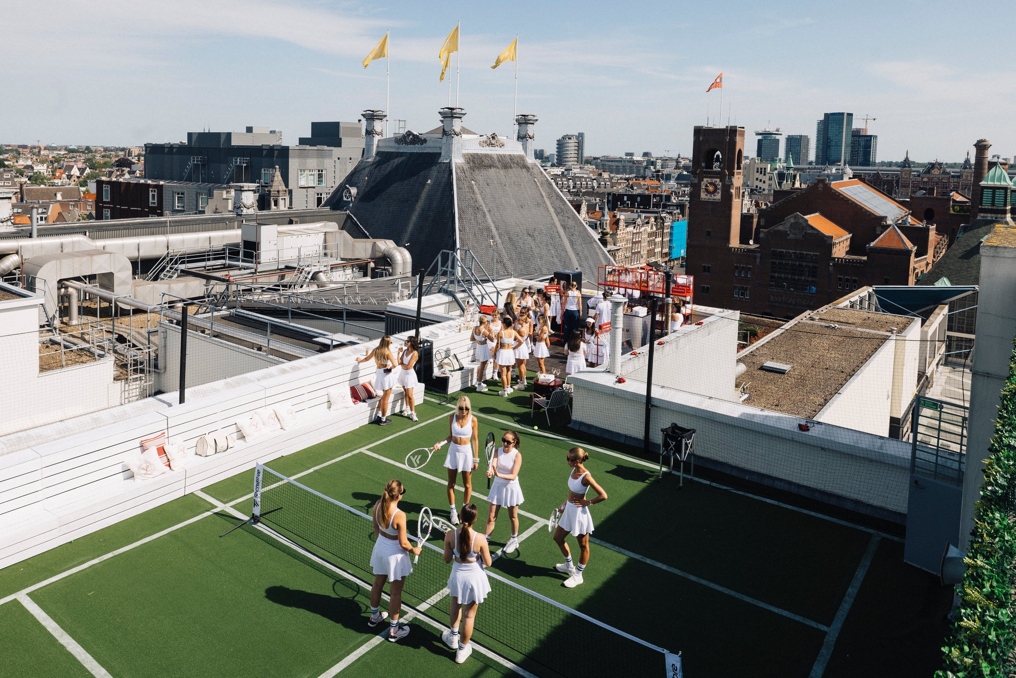 Tennisspel op de kunstgrasbaan op het dak van De Bijenkorf met de Amsterdamse skyline op de achtergrond. Foto: Kirsten van Santen